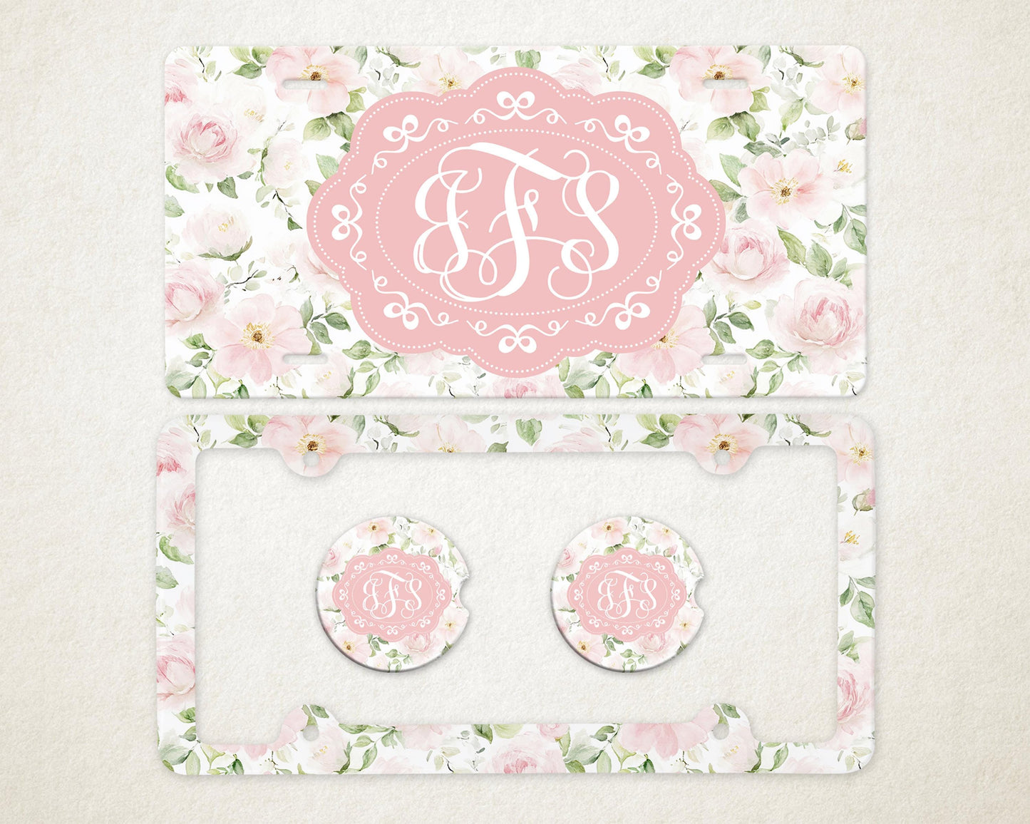 May include: A license plate and car accessories set featuring a floral design with pink roses and green leaves. The set includes a license plate, a license plate frame, and two car coasters. Each item has a pink oval with white initials.