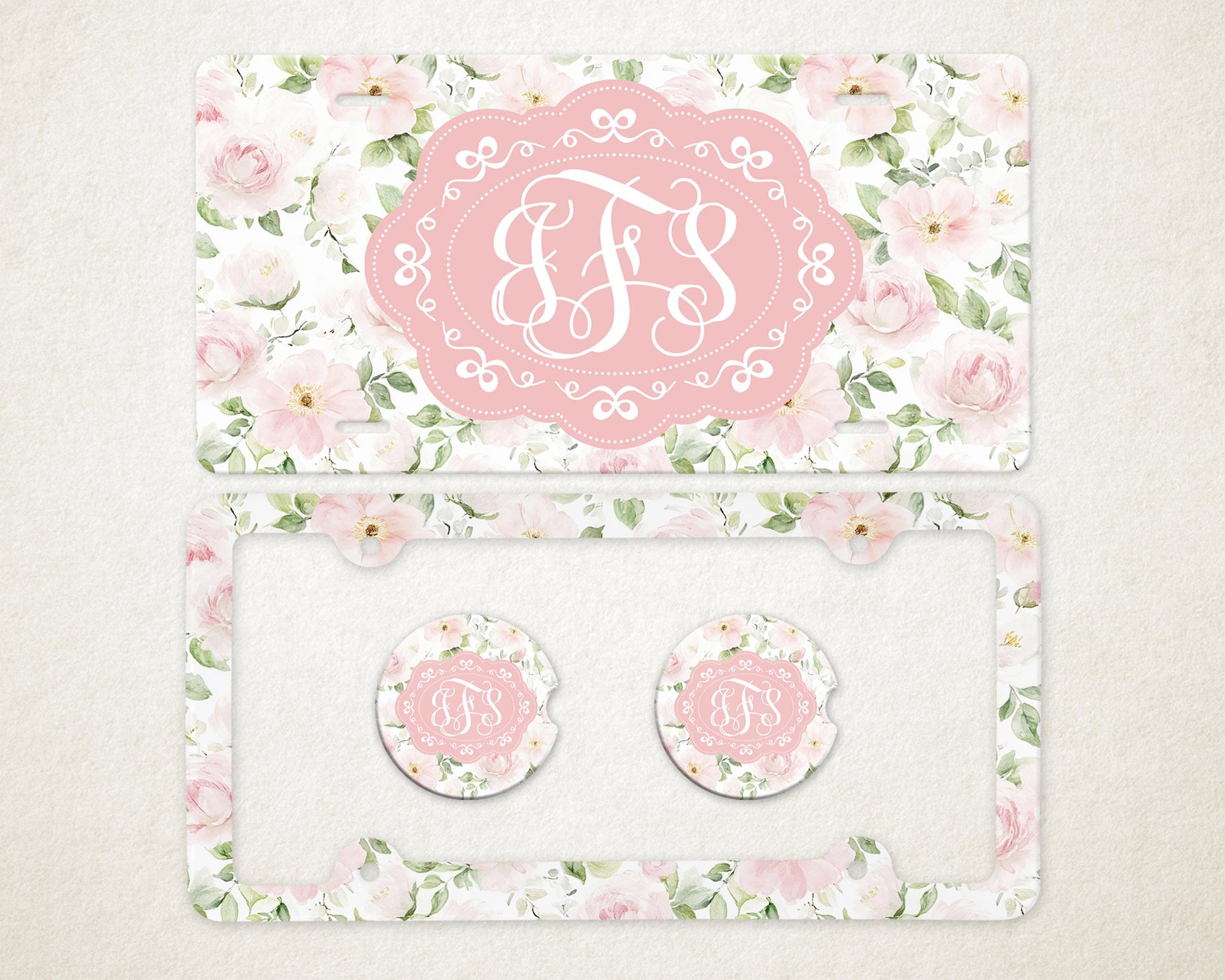 May include: A license plate and car accessories set featuring a floral design with pink roses and green leaves. The set includes a license plate, a license plate frame, and two car coasters. Each item has a pink oval with white initials.
