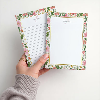 May include: Two floral notepads with a gold border and the name "Jenna Finley" printed at the top. One notepad has lined paper, and the other is blank. The floral design features pink flowers and green leaves.